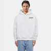 Sweat à capuche blanc avec logo noir "TOURISMO", porté par un homme en jean clair sur fond blanc lumineux