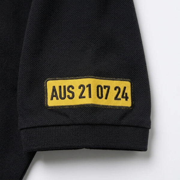 Gros plan sur la plaque AUS 21 07 24 brodée sur la manche du polo noir