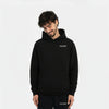 Homme souriant portant un hoodie noir TOURISMO et un pantalon assorti, regard vers le bas